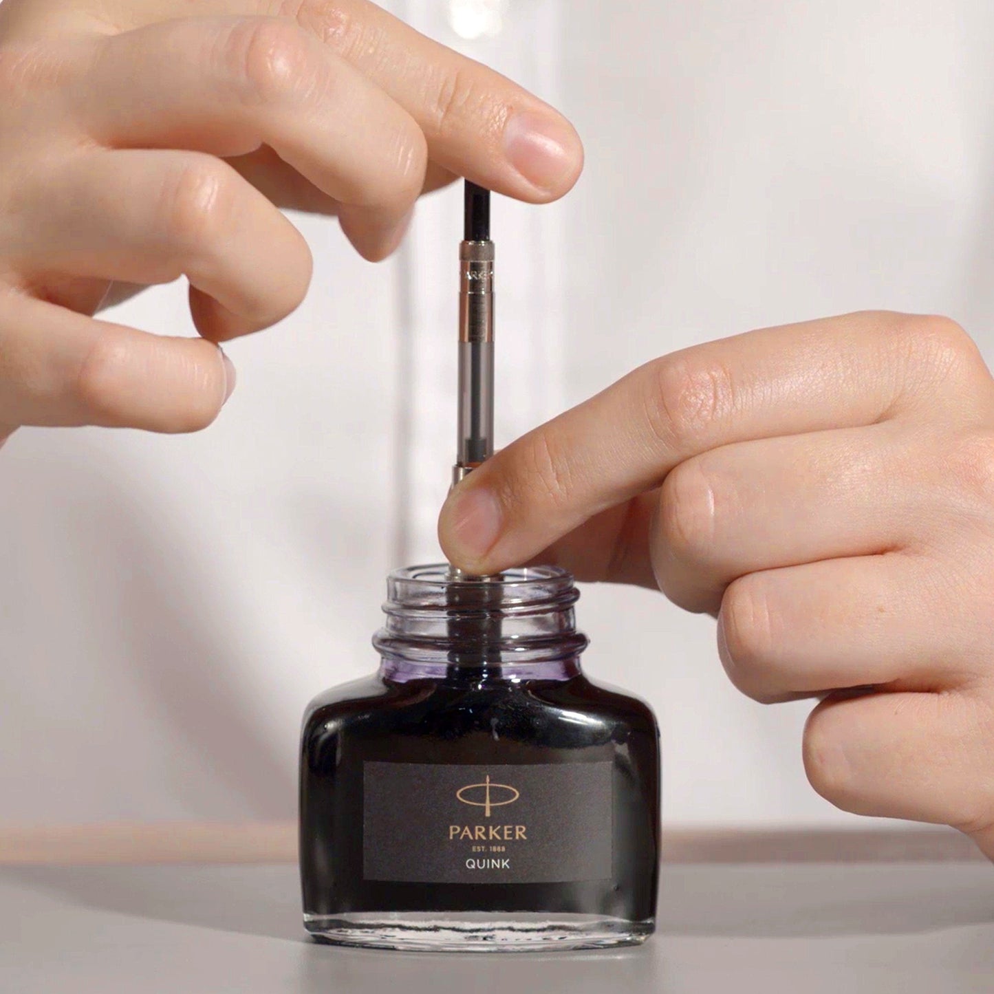 Person filling a Parker pen nib with a Parker Quink ink bottle.