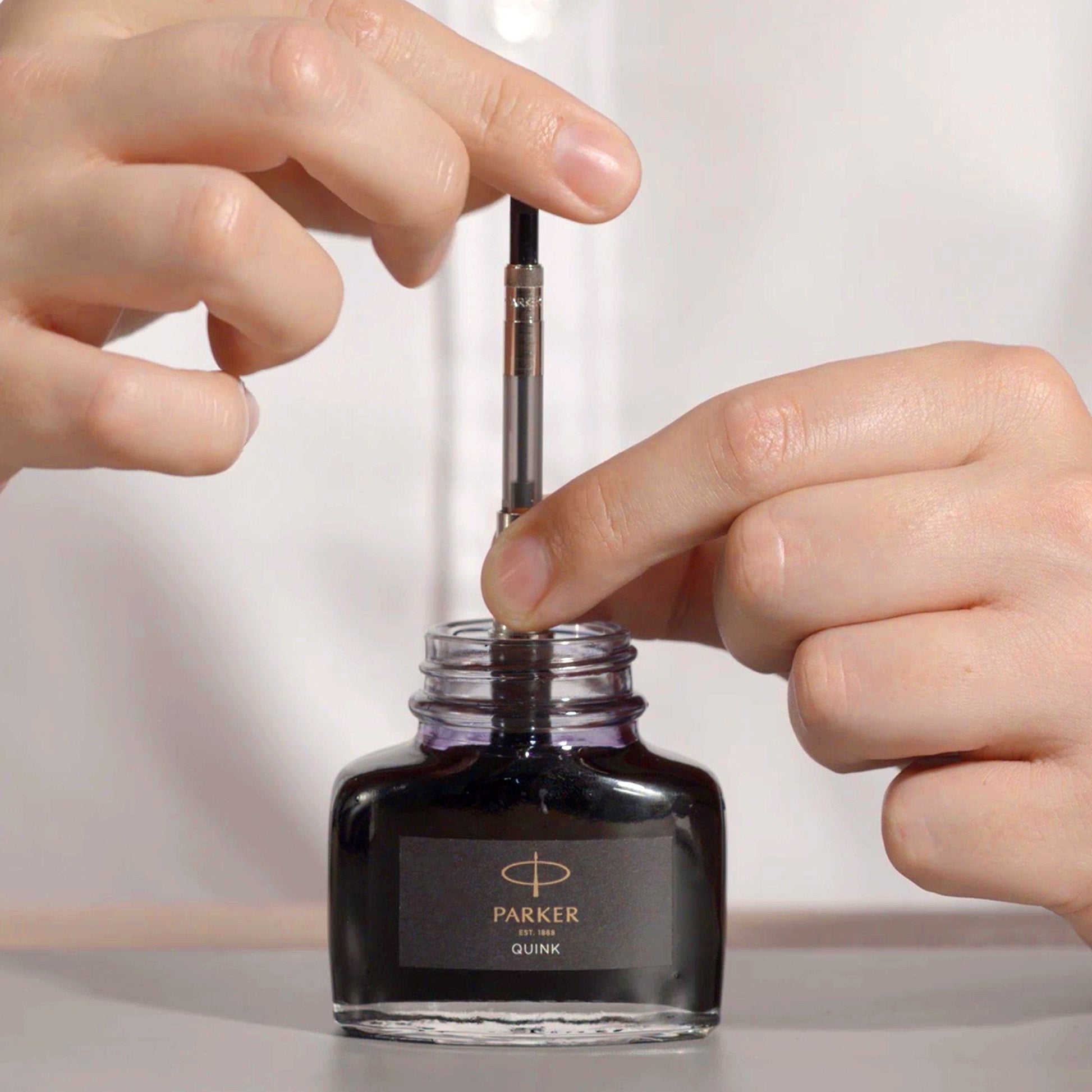 Person filling a Parker pen nib with a Parker Quink ink bottle.